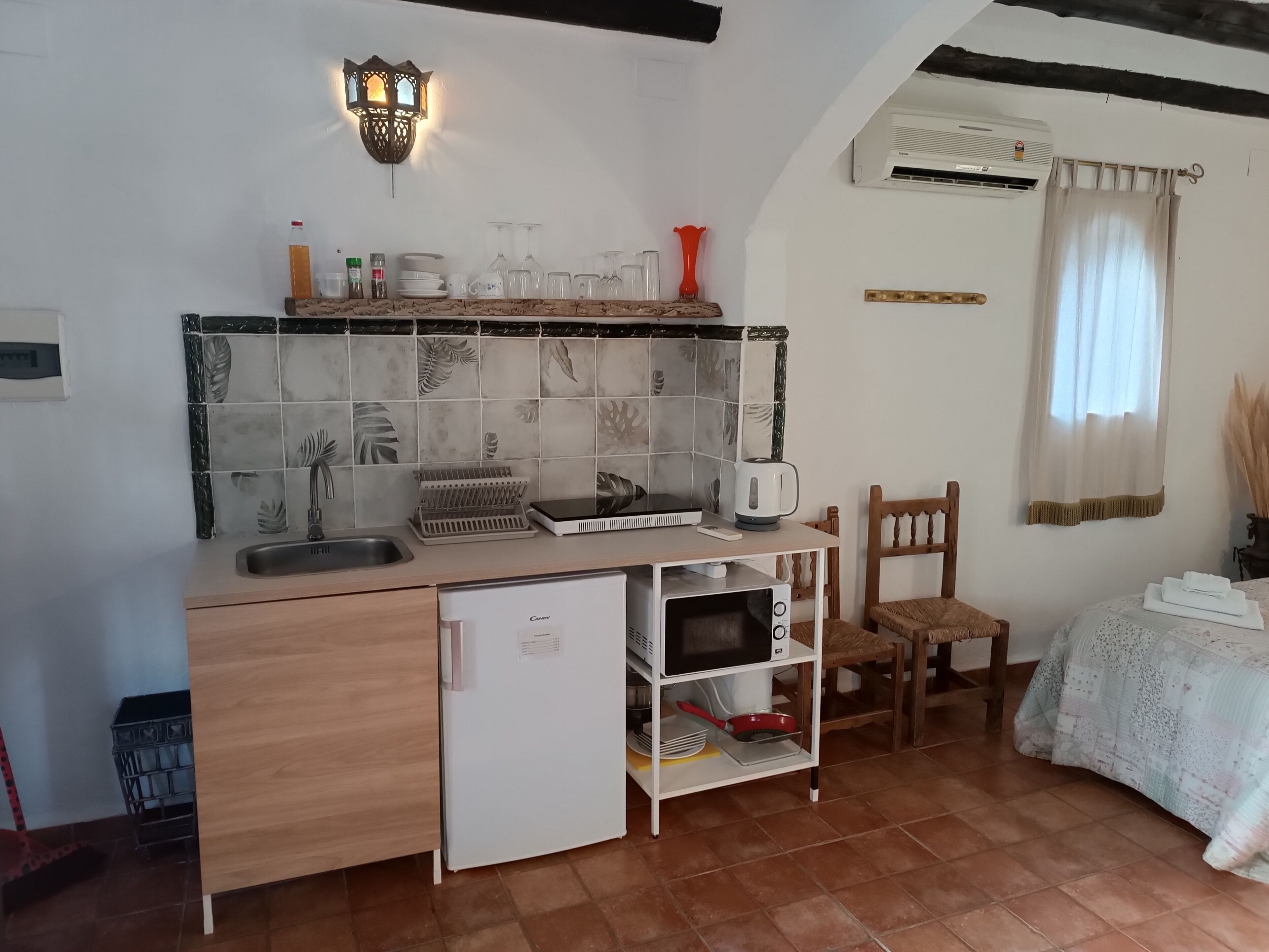 A compact kitchen with a built-in refrigerator, a microwave, and a coffee maker. There is a small sink and a shelf with kitchenware.