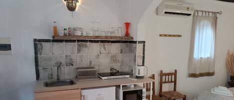 A compact kitchen with a built-in refrigerator, a microwave, and a coffee maker. There is a small sink and a shelf with kitchenware.