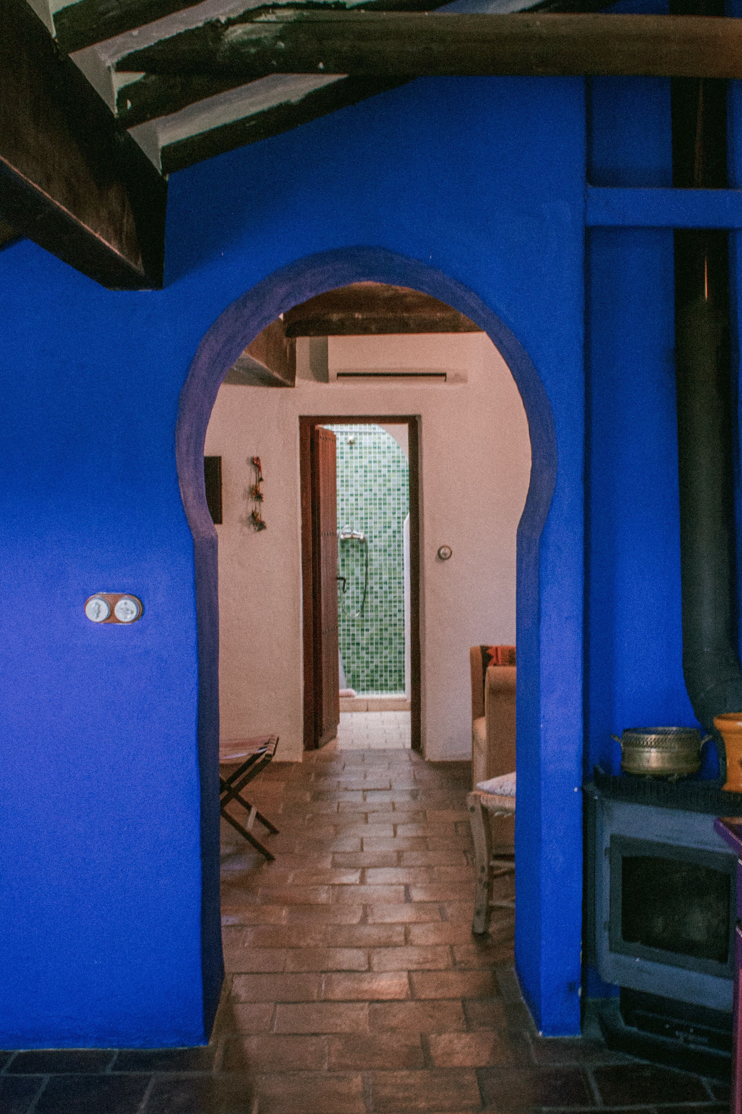 A narrow hallway with a blue archway leading to a room with a tiled floor and a fireplace.