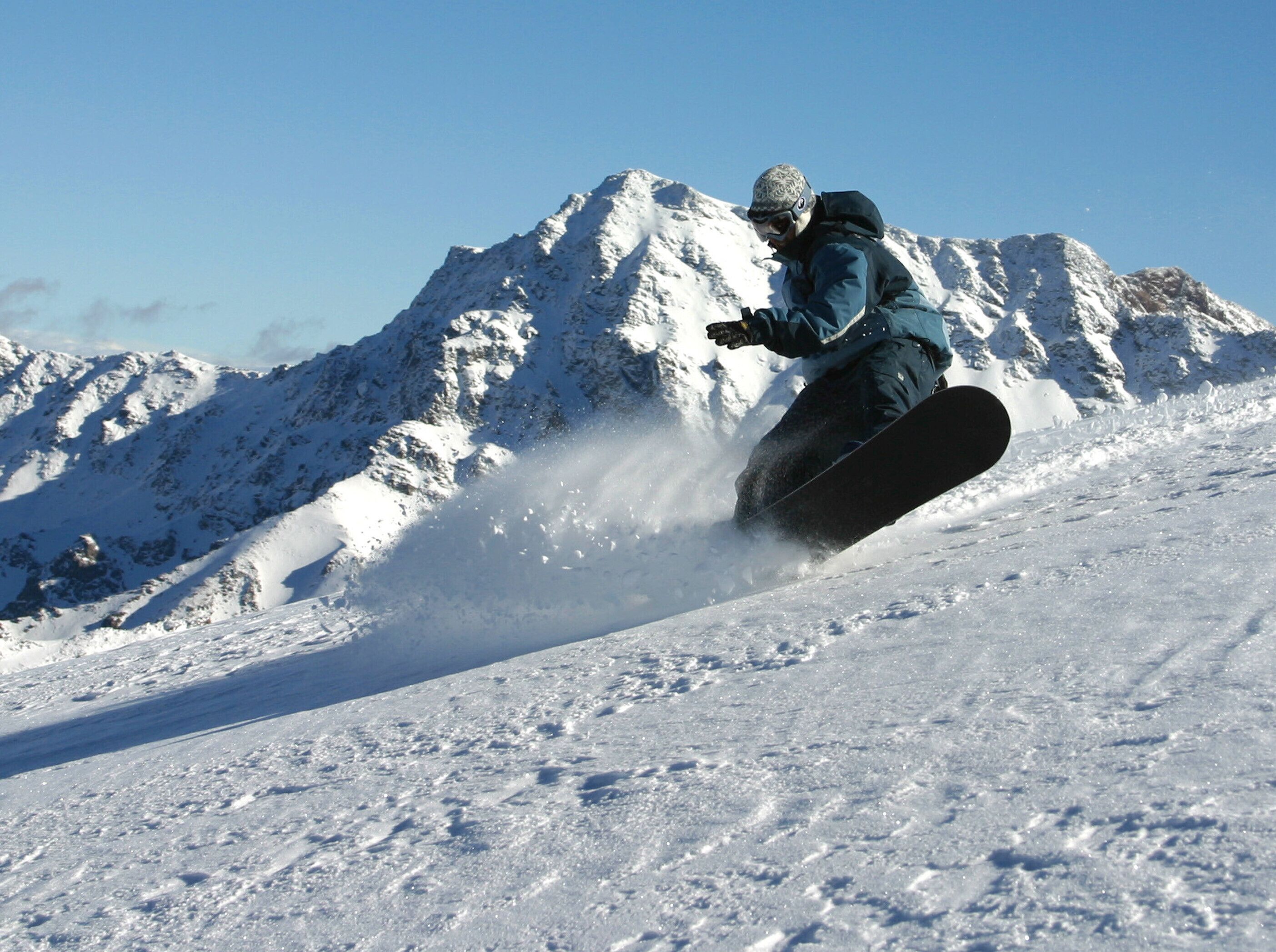 En snowboarder styrter ned ad en sneklædt skråning med et bjerg i baggrunden.