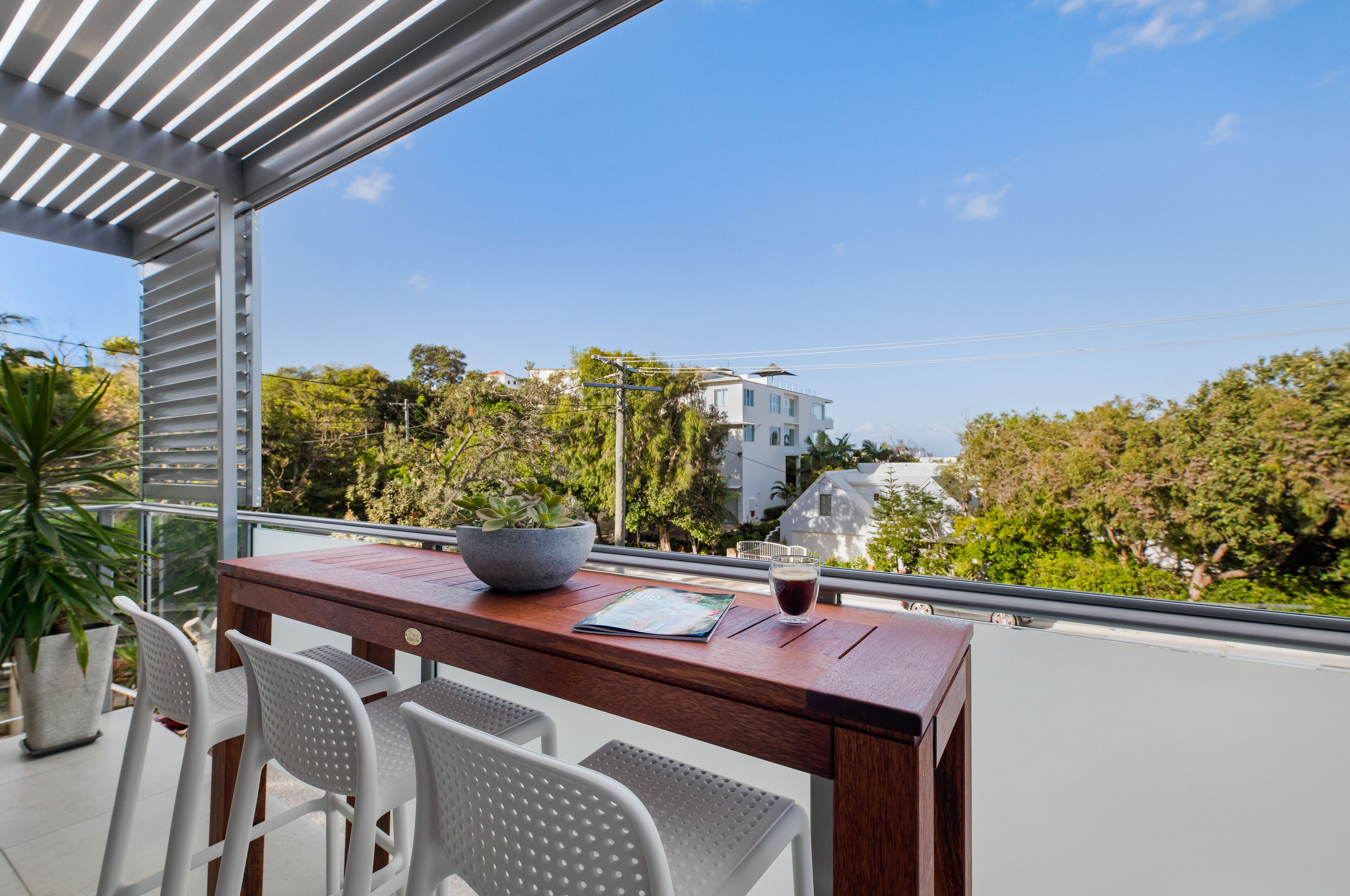 A balcony with a wooden table, white chairs, a bowl, and a glass of beverage.