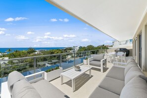 Un balcon extérieur moderne doté d’une balustrade en verre, de mobilier blanc et offrant une vue sur la mer.