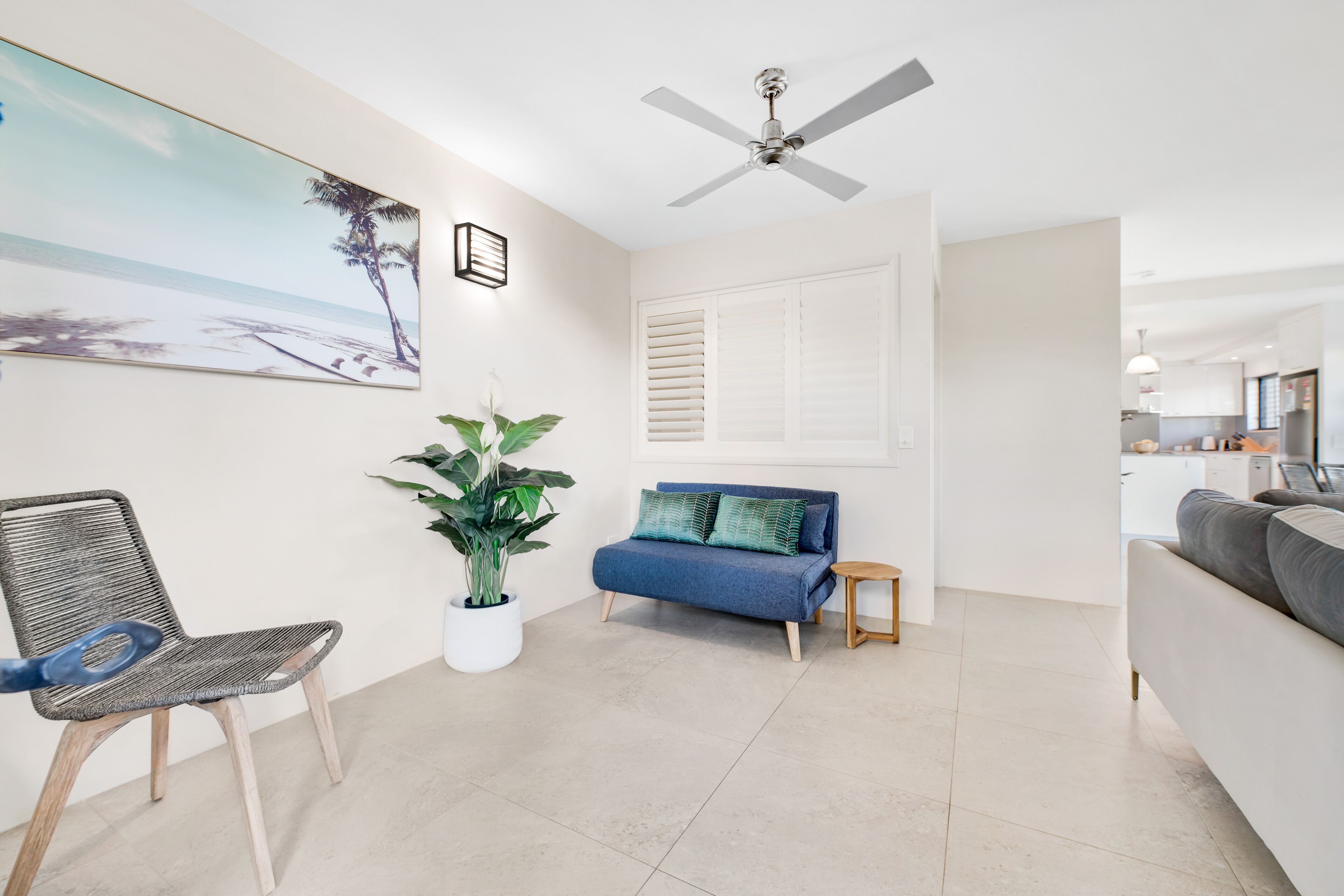 A modern living room with a sofa, a chair, a ceiling fan, a potted plant, and a painting on the wall.