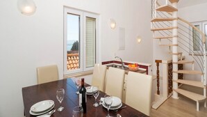Un comedor con una mesa de madera preparada para cuatro, una cocina con frutero y una escalera de caracol.