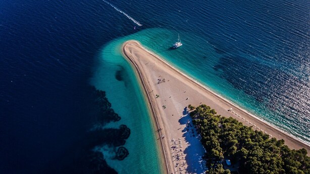 Vista aérea de una playa con aguas cristalinas, un bote y una línea de árboles densa.