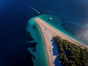 An aerial view of a beach with clear waters, a boat, and a dense tree line. - Villa Balarin (Bol)