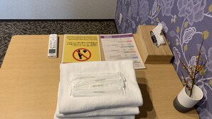 Habitación de hotel con una mesa de madera, un cartel con el símbolo de prohibido fumar, un menú, una caja de pañuelos, un portalápices para cepillos de dientes y un florero con una rama.