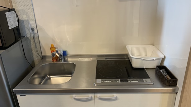 Una kitchenette compacta con un lavamanos de acero inoxidable, una estufa integrada y un refrigerador pequeño.