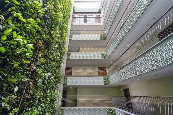 A multi-level atrium with a central staircase, balconies with railings, and a lush green wall.