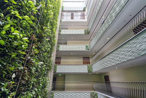 A multi-level atrium with a central staircase, balconies with railings, and a lush green wall.