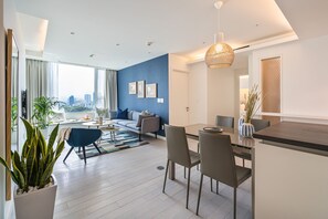 A modern living room with a sofa, dining table, and chairs. There is a large window with curtains, a potted plant, and a city view. - Saigon Finest - IDG Suites Collection - 12J (Ho Chi Minh City)
