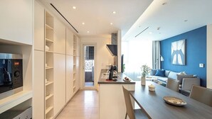 A modern kitchen with built-in appliances, a dining area with a wooden table, and a living room with a blue accent wall. - Saigon Finest - IDG Suites Collection - 12J (Ho Chi Minh City)