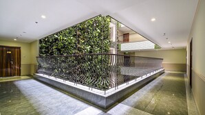 Een moderne hotel lobby met een centrale trap, een glazen wand met beplanting en een gepolijste marmeren vloer.