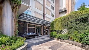 A modern building with a car parked in front, a paved walkway, and greenery around. - Saigon Finest - IDG Suites Collection - 12K (Ho Chi Minh City)