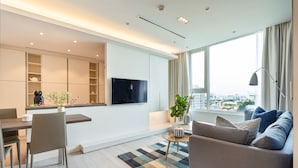 A modern living room with a sofa, a dining area, and a TV mounted on the wall. - Saigon Finest - IDG Suites Collection - 12K (Ho Chi Minh City)