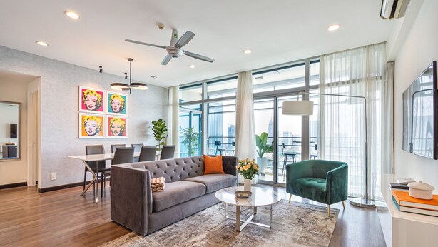 A modern living room with a grey sofa, a green armchair, a round coffee table, and a city view through large windows. - Saigon Skyline Suite in Central District 1 (Ho Chi Minh City)