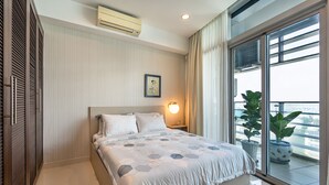 A modern hotel room with a large bed, a bedside table with a lamp, a potted plant, and a view of the city through large windows. - Sai Gon Finest - Panorama Suite in Central D1 (Ho Chi Minh City)