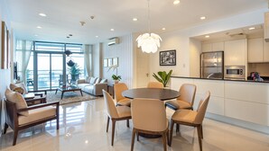A modern living room with a dining area, large windows, and a kitchen with stainless steel appliances. - Sai Gon Finest - Panorama Suite in Central D1 (Ho Chi Minh City)