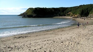 A sandy beach with gentle waves, a rocky cliff, and a clear sky.