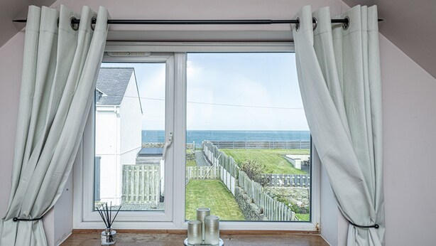A room with a large window, white curtains, and a wooden shelf with candles.