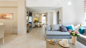 A modern living room with a grey sofa, a coffee table with candles and flowers, and a dining area in the background. - Peris Villa (Chania)