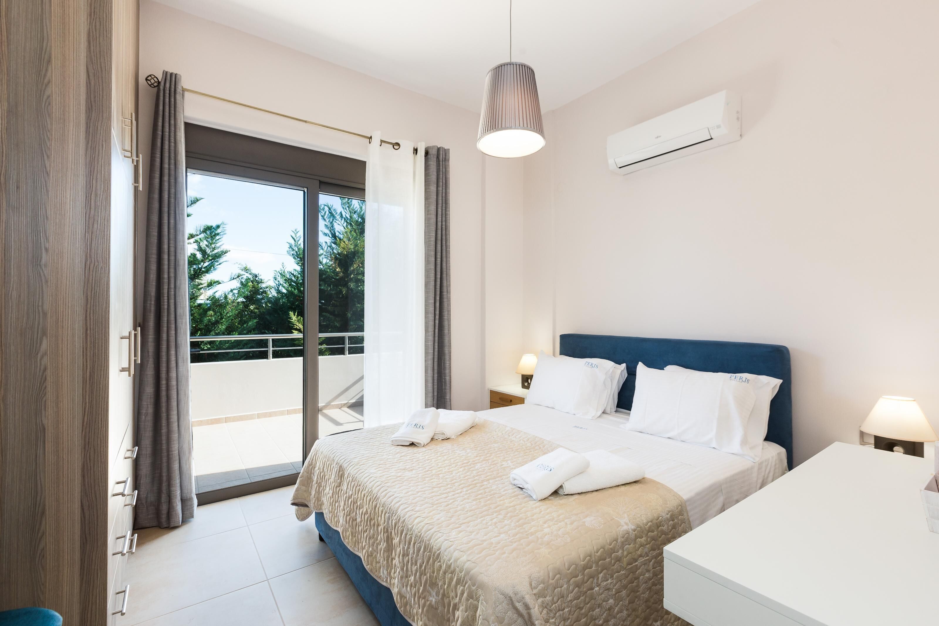 A modern hotel room with a large bed, a desk, and a balcony with curtains.