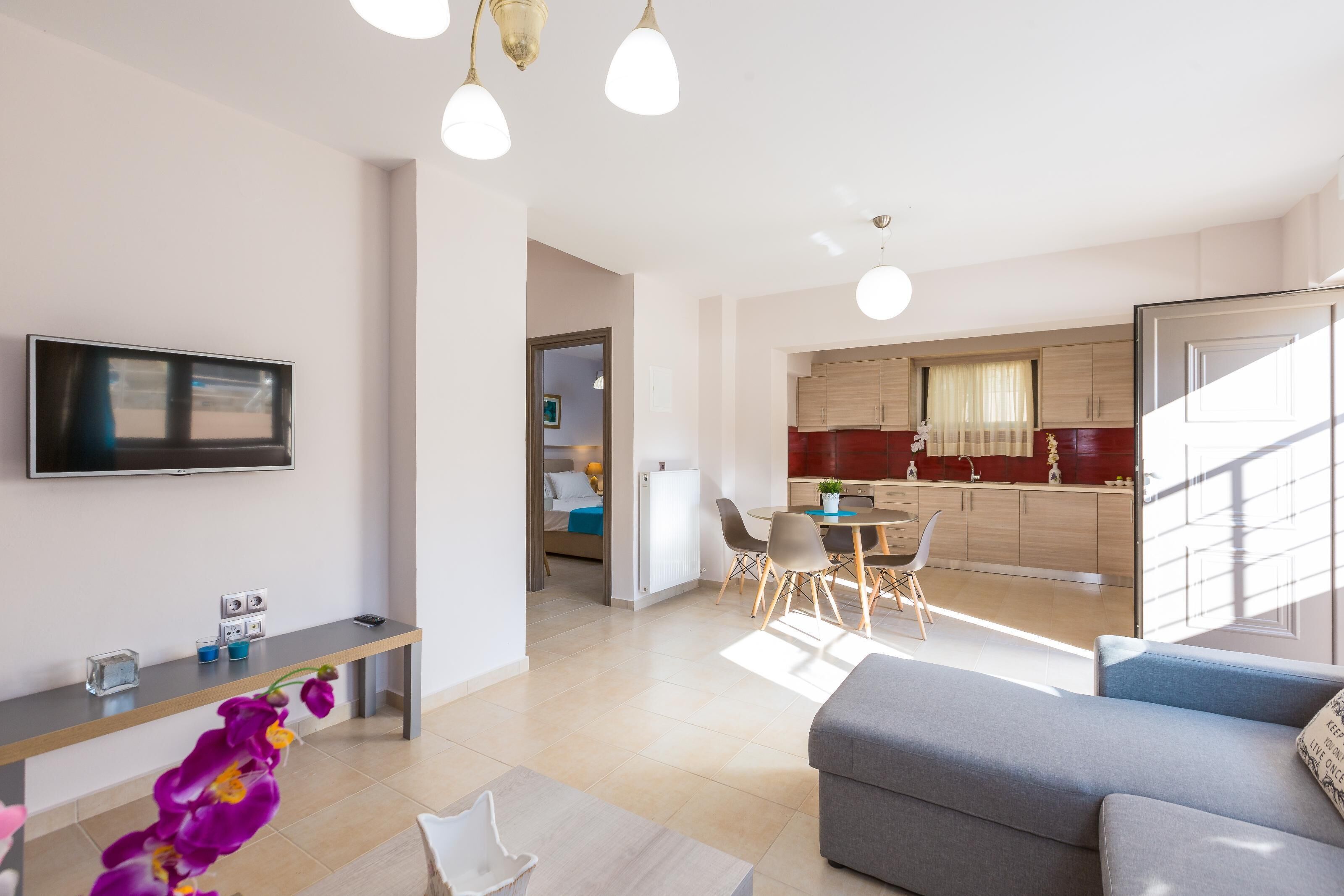 A modern living room with a flat-screen TV, a sofa, and a dining area with a table and chairs.