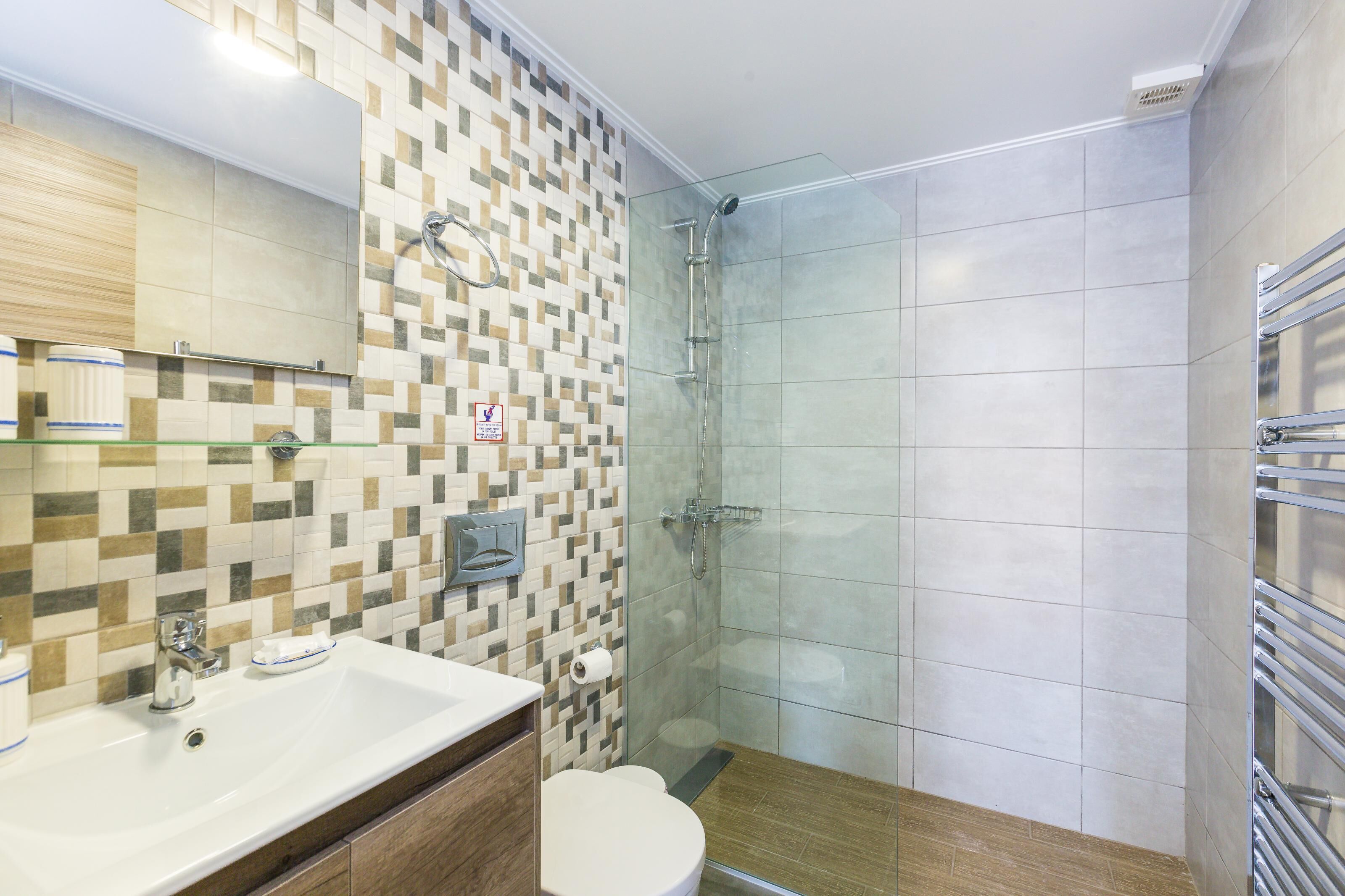 Ein modernes Badezimmer mit gefliester Dusche, Waschbecken mit Spiegel und Toilette.