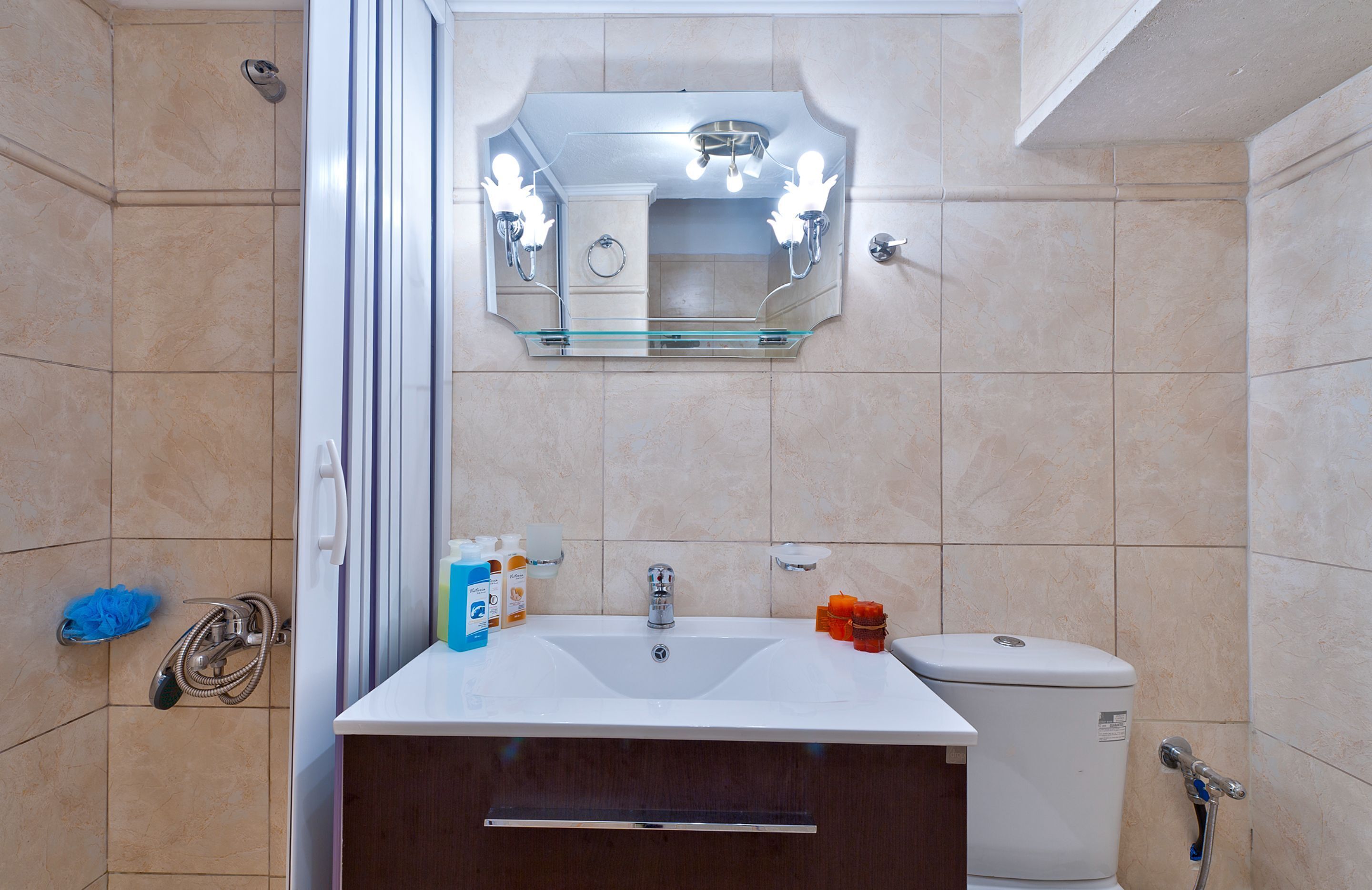 A bathroom with a white sink, a mirror, and a toilet. There are toiletries on the sink and a showerhead on the wall.