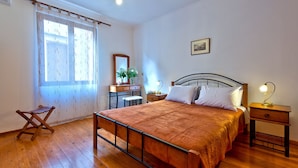 Un dormitori amb un llit de fusta, una taula de nit, un calaixera, una cadira, una finestra amb cortines i una làmpada al sostre.