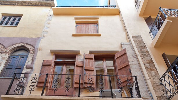 Un edifici amb un balcó, persianes de fusta i un gran portal d'arc.