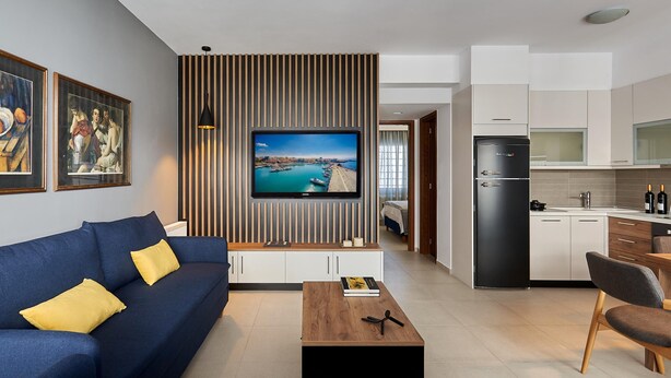 A modern living room with a blue sofa, wooden coffee table, and a TV mounted on a wall with vertical wooden slats. - Thalita Cozy Apartment (Heraklion)