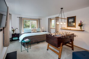 A bedroom with a bed, a desk, a foosball table, and a window.