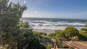 Vista costera con olas rompiendo en la orilla, rodeada de vegetación densa y un cielo despejado.