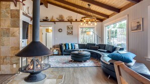 Una sala de estar acogedora con chimenea de piedra, un sofá seccional y un amplio ventanal que proporciona luz natural.