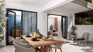 Ein moderner Essbereich mit Holztisch und Korbstühlen, einem kleinen Beistelltisch mit Kerzen und Blick auf den angrenzenden Wohnraum.