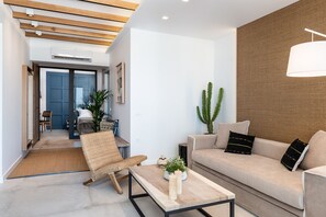 Una sala moderna con un sofá, una mesa de centro y un sillón. Hay una planta en la mesa de centro y un cactus en la pared.