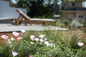 Un jardín con flores rosadas y una silla de lounge de madera.