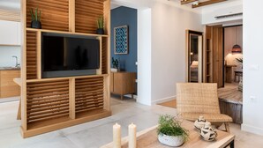 Ein modernes Wohnzimmer mit einem großen Flachbildfernseher, Holzvertäfelung, einer blauen Akzentwand, einem Korbstuhl und einem Essbereich mit Kerzen und Dekoration.