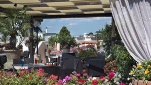 Ein Außenbereich mit Korbmöbeln, umgeben von bunten Blumen und Pflanzgefäßen.