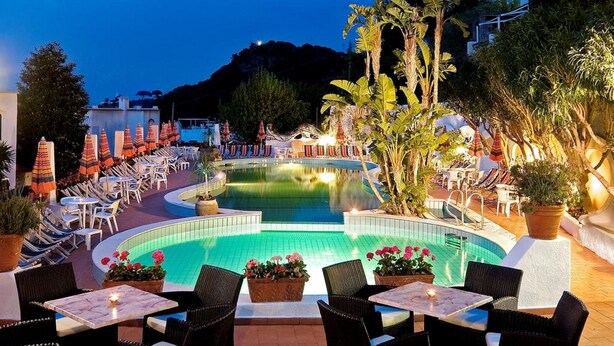 Ein Poolbereich mit Liegestühlen und Sonnenschirmen, umgeben von Blumentöpfen und Blick auf den Pool.