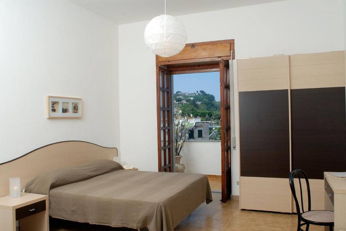 A bedroom with a bed, bedside table, and a view through an open door to a balcony.