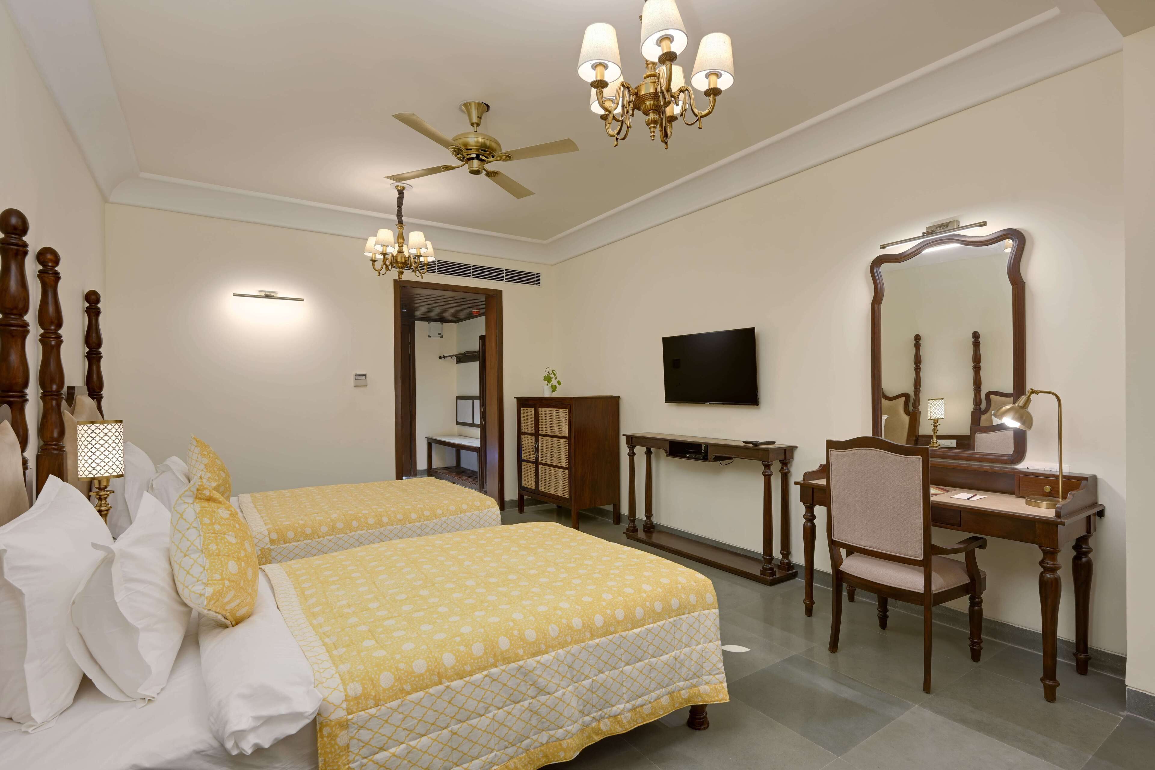 A hotel room with two beds, a desk with a chair, a television, and a large mirror.