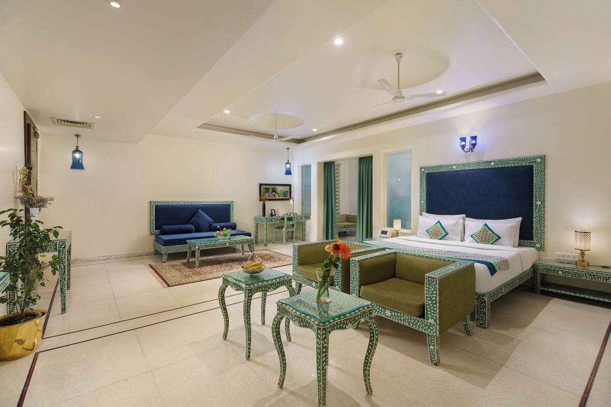 Una habitación de hotel con cama, sofá, dos mesas, una silla y una planta en maceta.