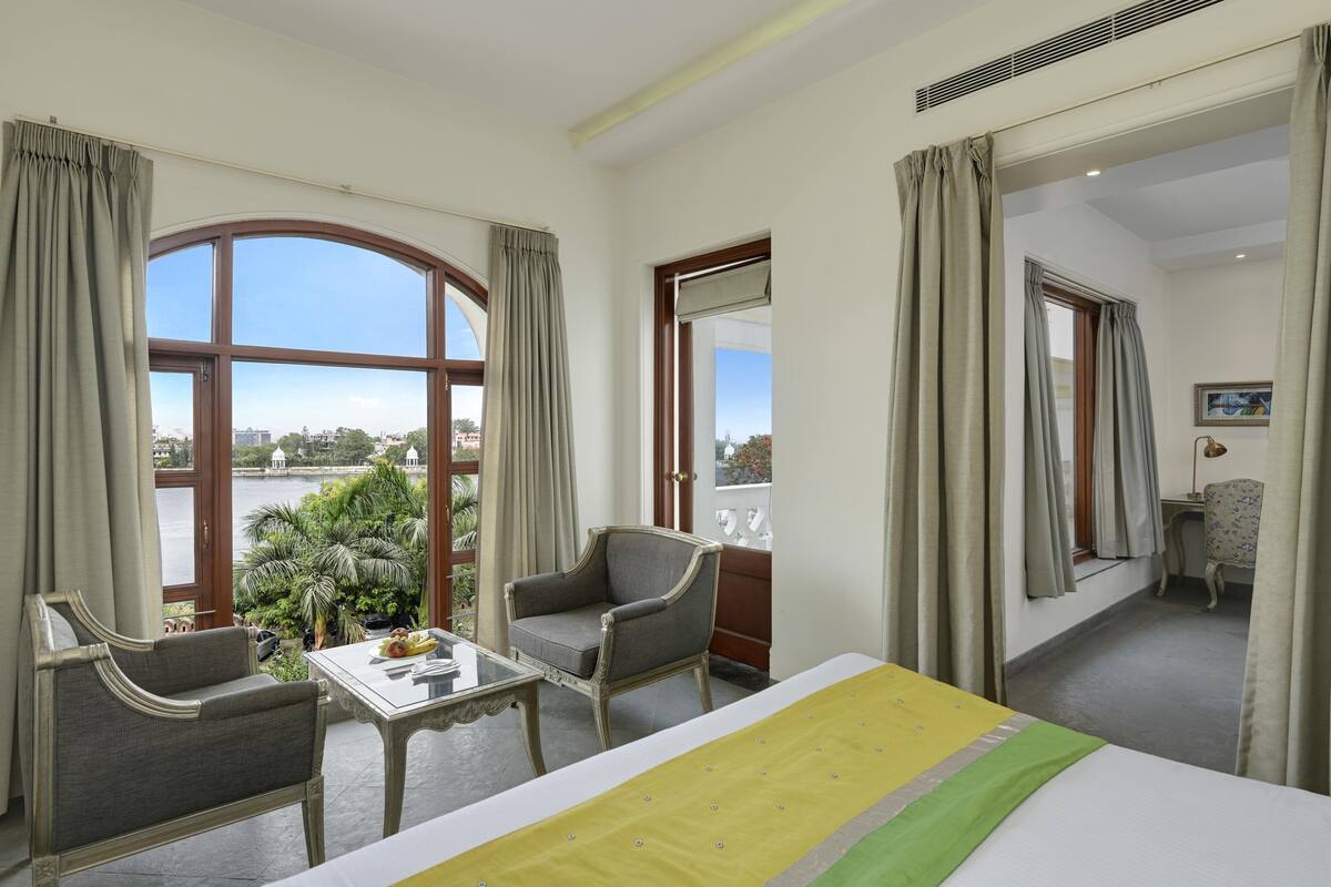 Habitación de hotel con cama, una mesa, dos sillas y vista a un cuerpo de agua y follaje.