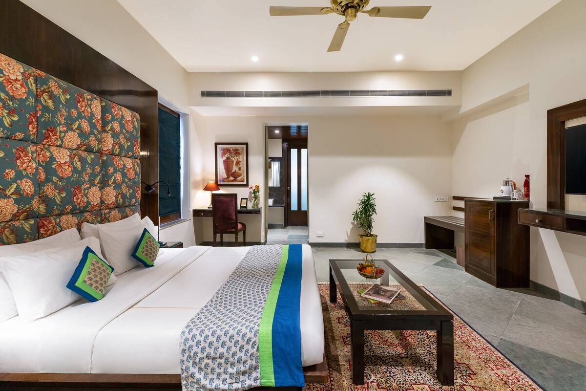 Habitación de hotel con una cama grande, un escritorio, una silla, una pequeña mesa con una planta y un televisor.