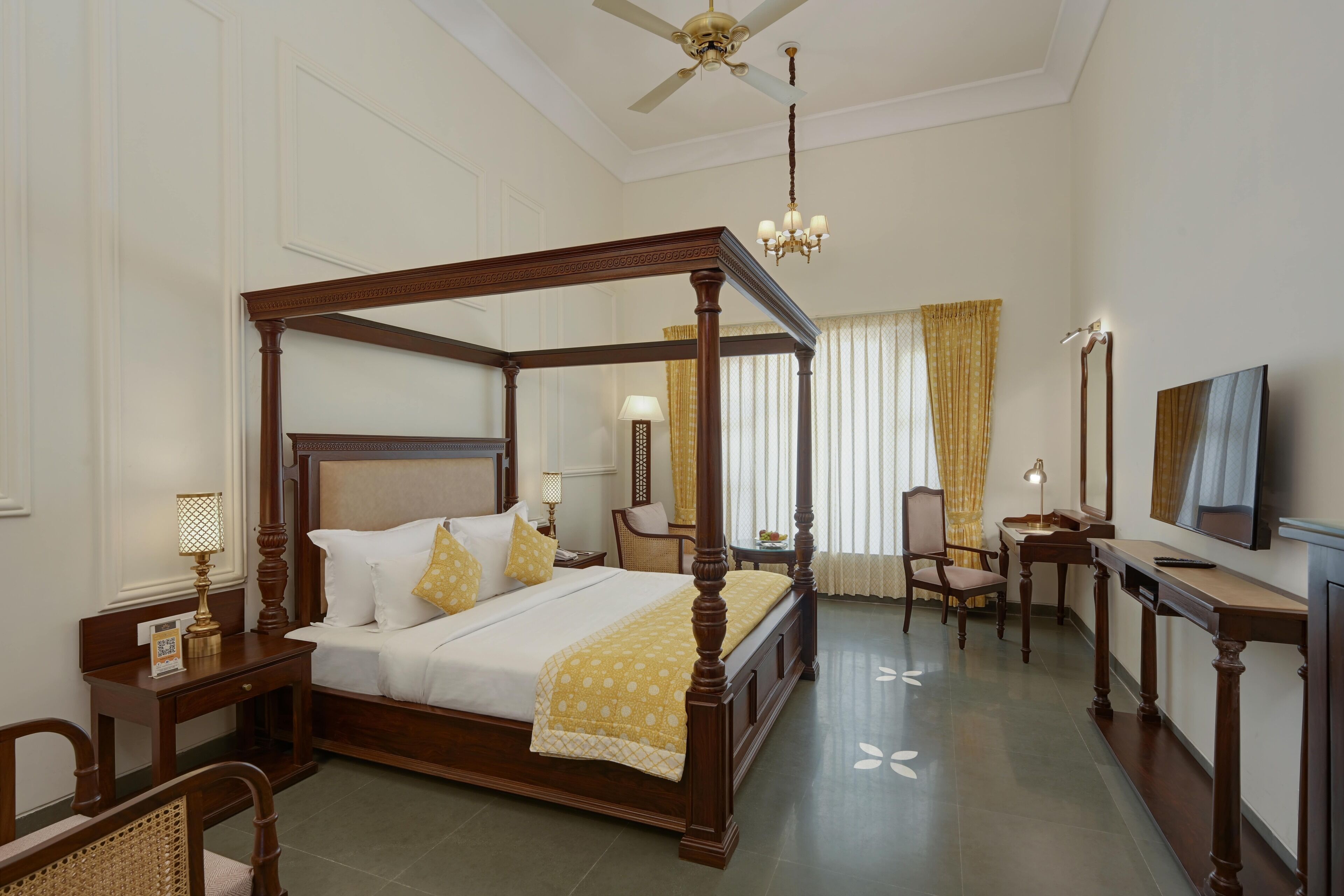 A four-poster bed with a wooden frame, a desk with a chair, a television, and a chandelier.