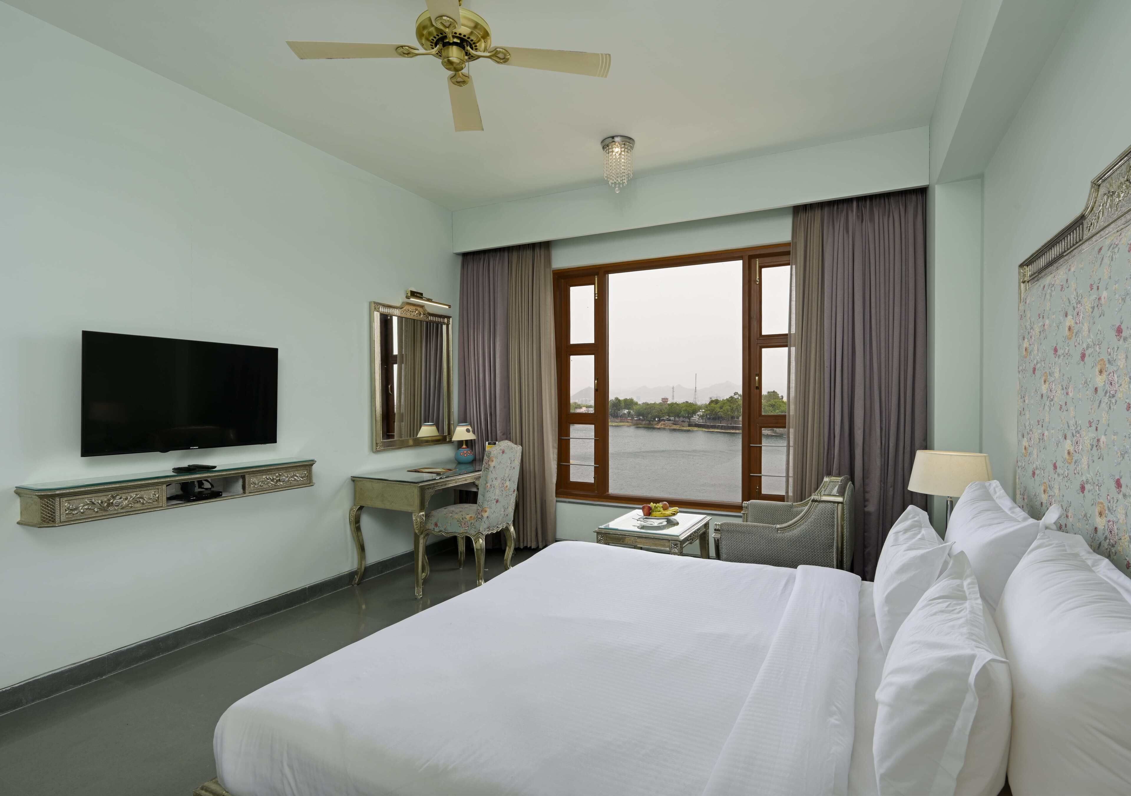 A hotel room with a bed, a desk, a television, a chair, and a view of the water.