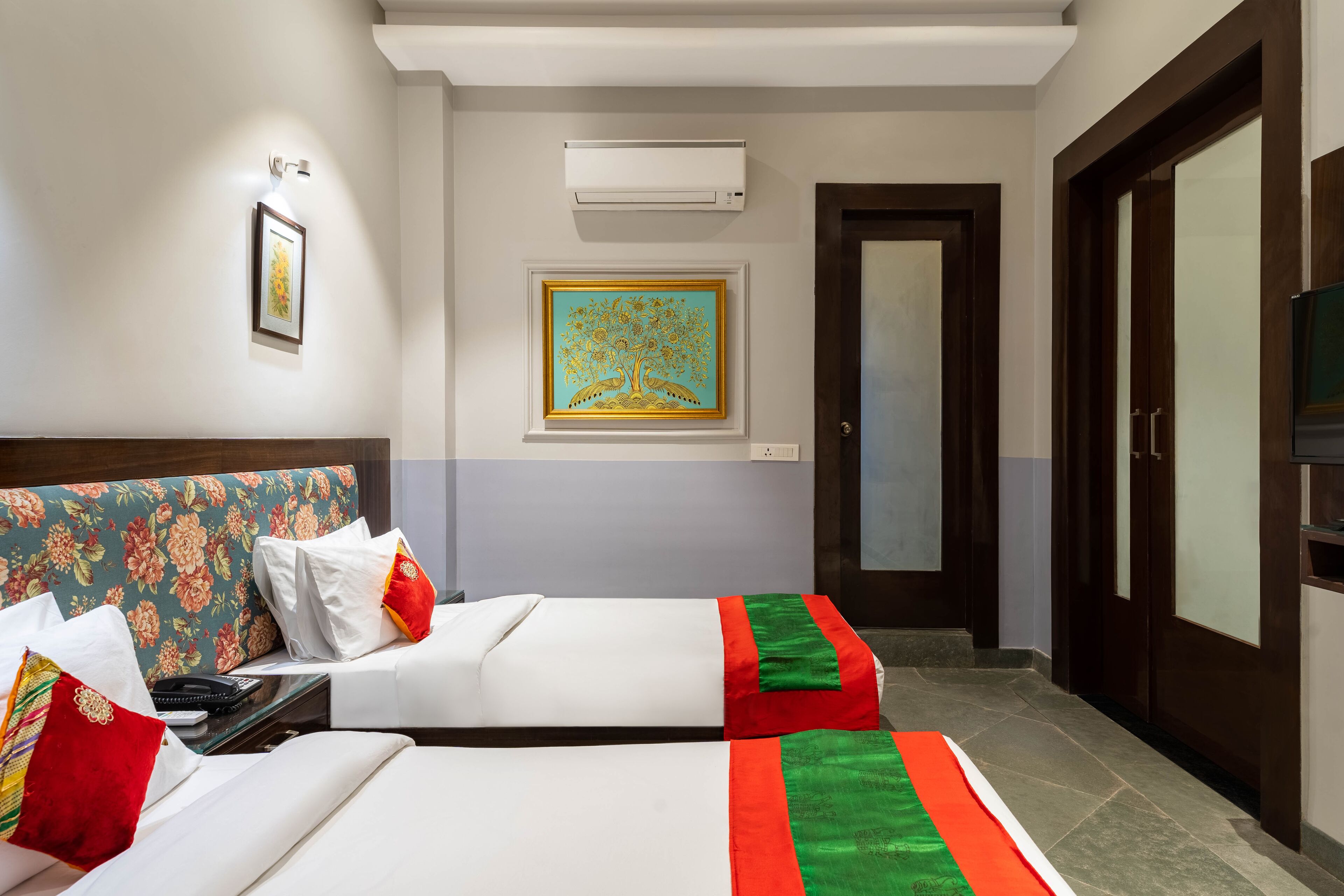 A hotel room with two beds, a large painting on the wall, an air conditioning unit, and a television.