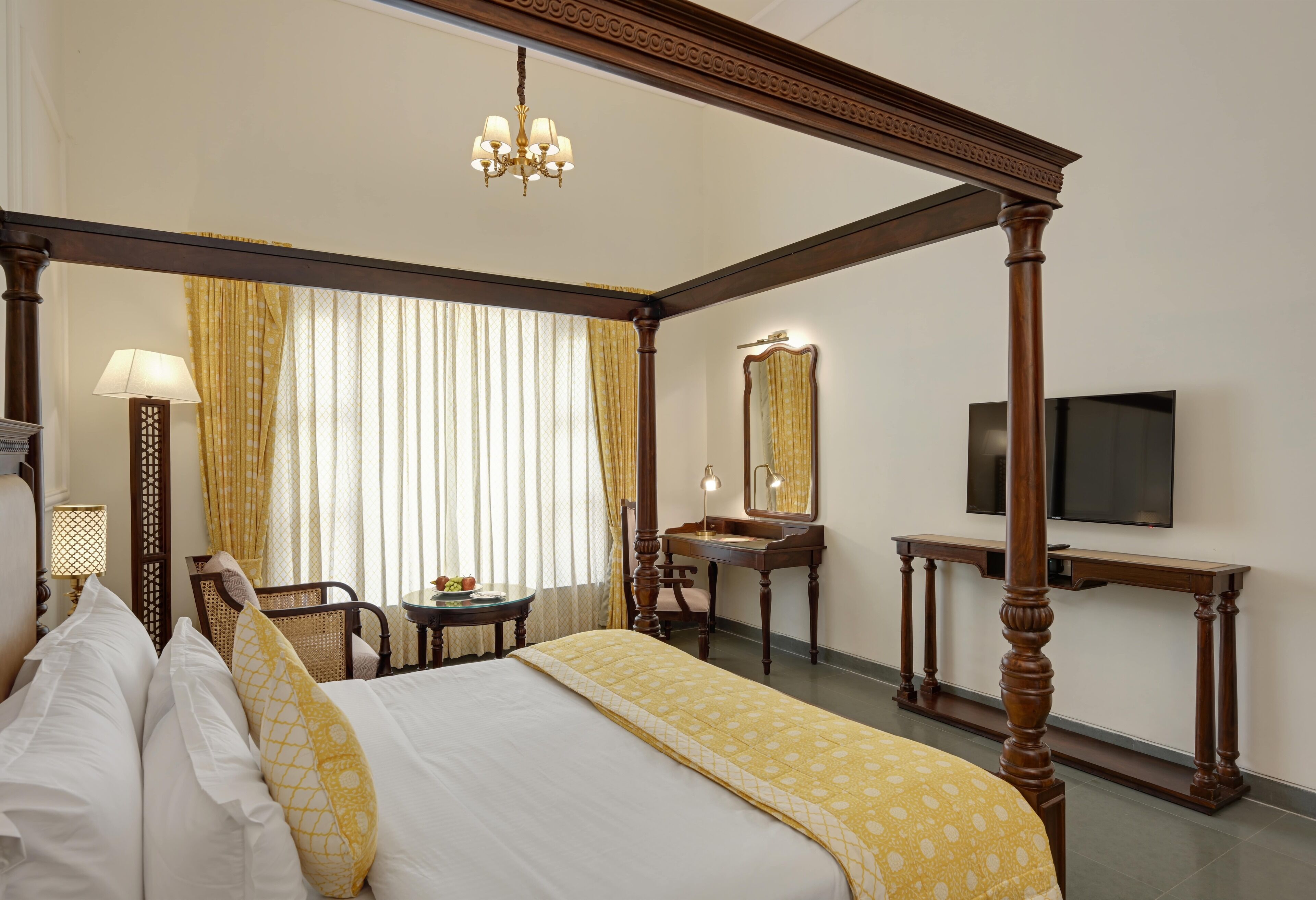 A four-poster bed with a wooden frame, a bedside table with a lamp, a mirror, and a television on a stand.